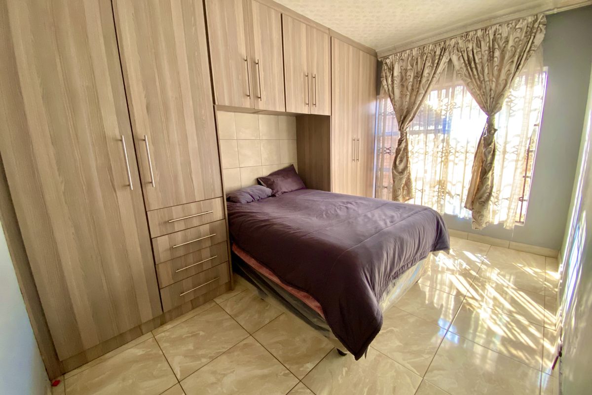 A bedroom featuring extensive built-in wooden cabinetry, tiled flooring, and natural light through a window with security gate.