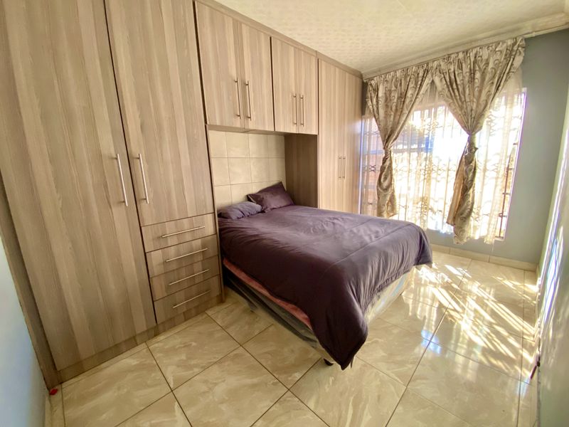 A bedroom featuring extensive built-in wooden cabinetry, tiled flooring, and natural light through a window with security gate.