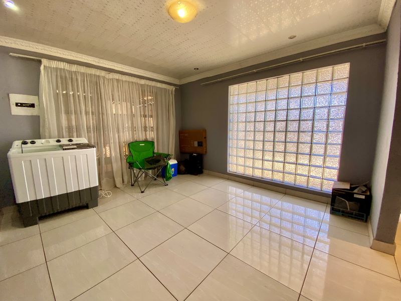 A spacious living area featuring large format floor tiles, a distinctive glass block feature window, and decorative ceiling cornicing.