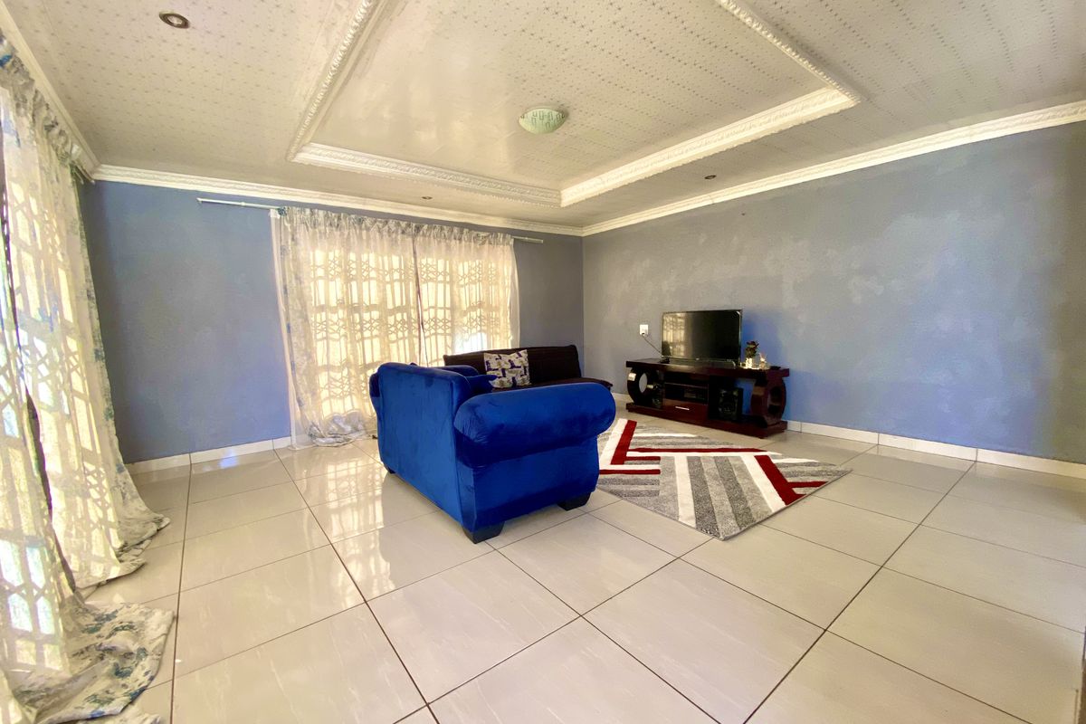 Spacious living room featuring tiled flooring, a decorative recessed ceiling with downlights, and large windows allowing for natural light.