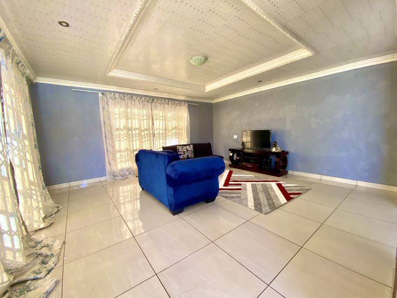 Spacious living room featuring tiled flooring, a decorative recessed ceiling with downlights, and large windows allowing for natural light.