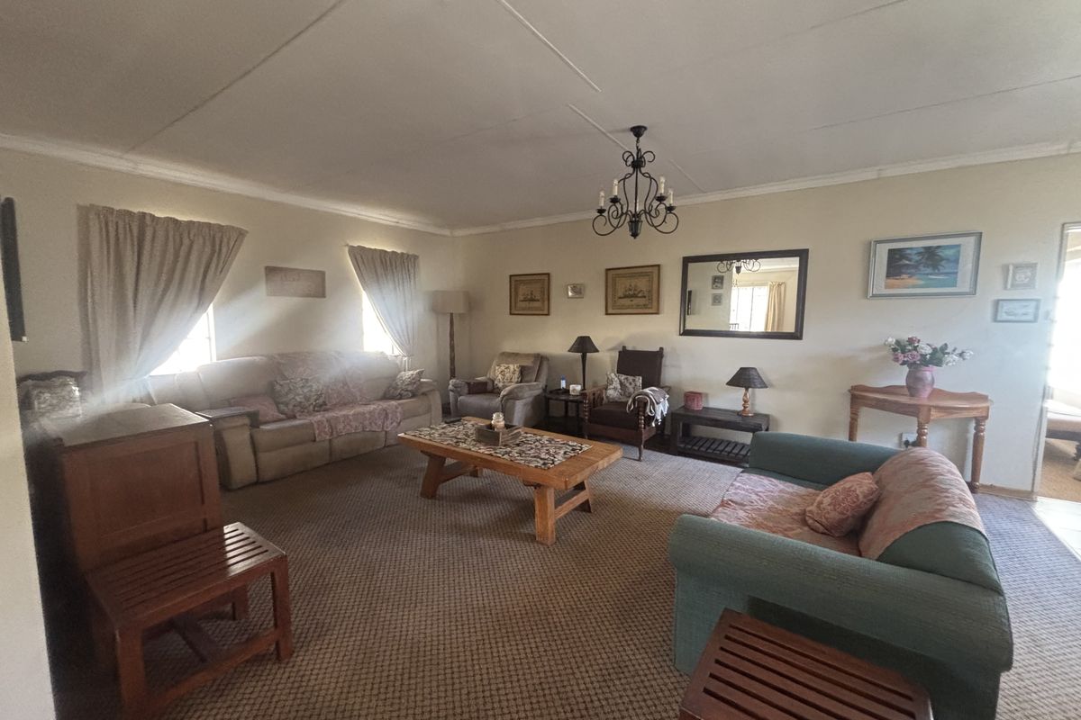A spacious living room featuring a traditional chandelier, coved ceilings, and carpeted flooring, offering a comfortable layout for family relaxation.