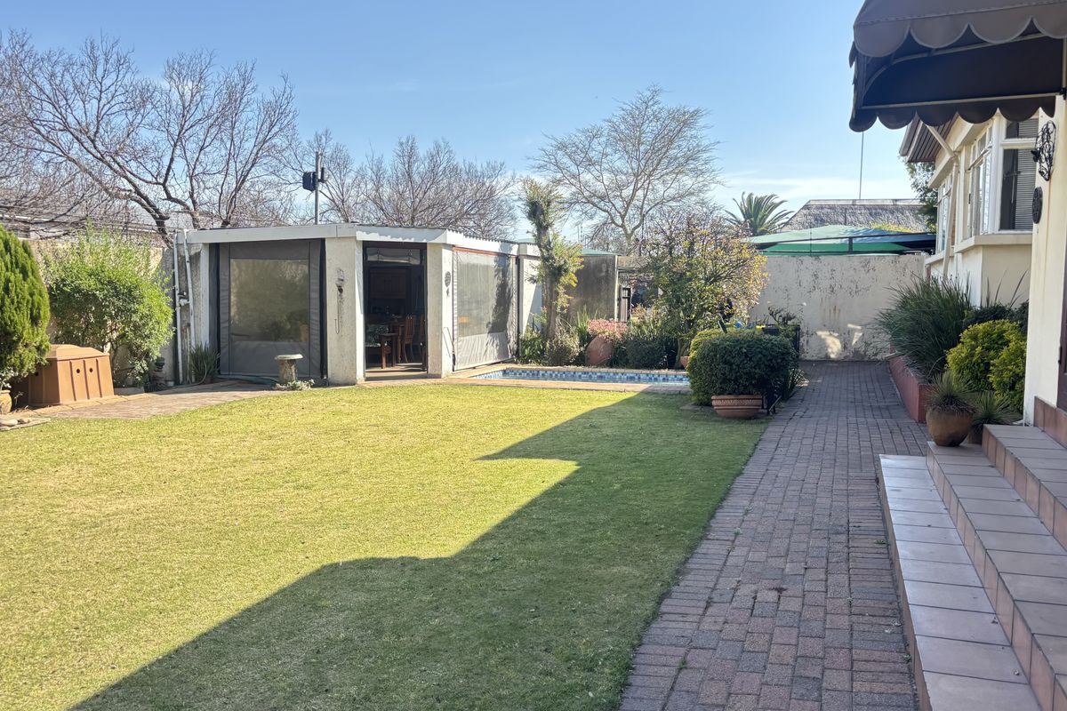 A spacious rear garden featuring a well-maintained lawn, a swimming pool, and a paved walkway leading to a covered patio area.