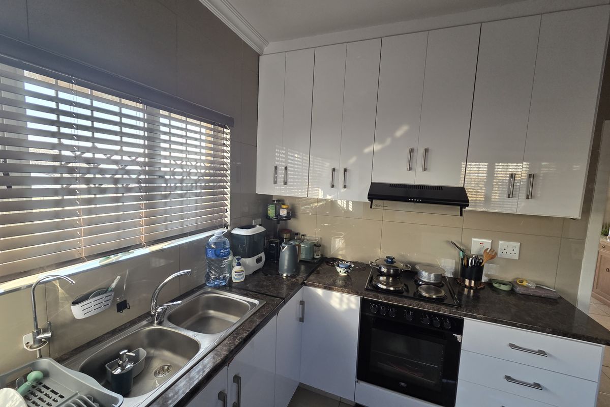 Modern kitchen featuring white gloss cabinetry, dark laminate countertops, a double bowl sink, and integrated cooking appliances with a tiled splashback.
