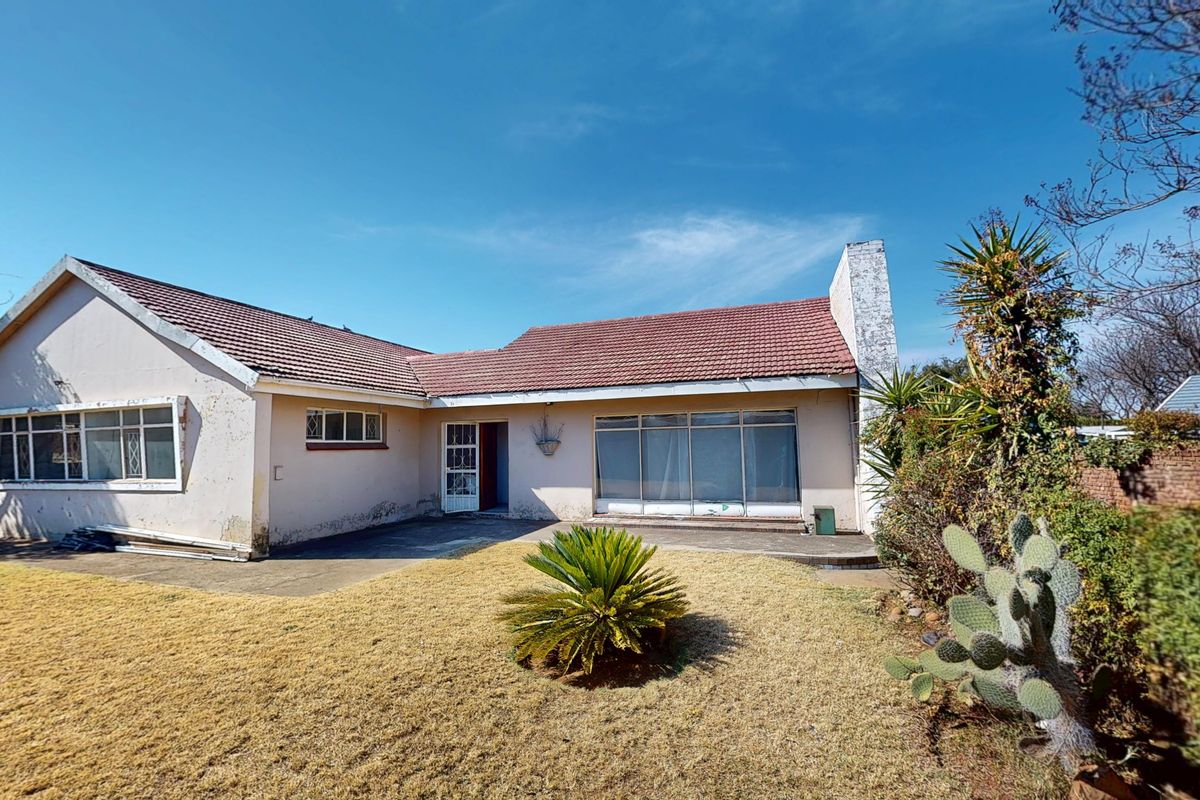 Rear view of a single-story house featuring a tiled roof, brick chimney, and a concrete patio area overlooking the garden.
