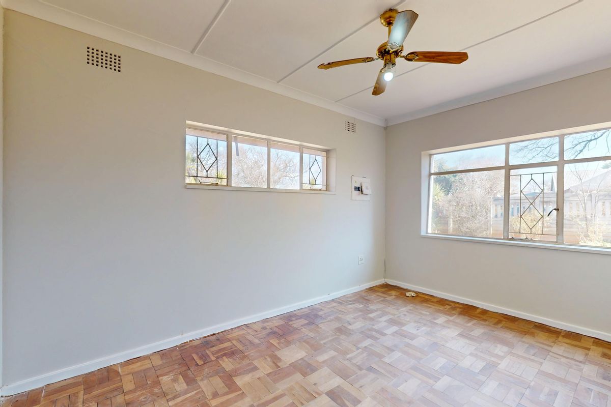 An empty bedroom featuring original parquet flooring, a ceiling fan, and large steel-framed windows with security bars.