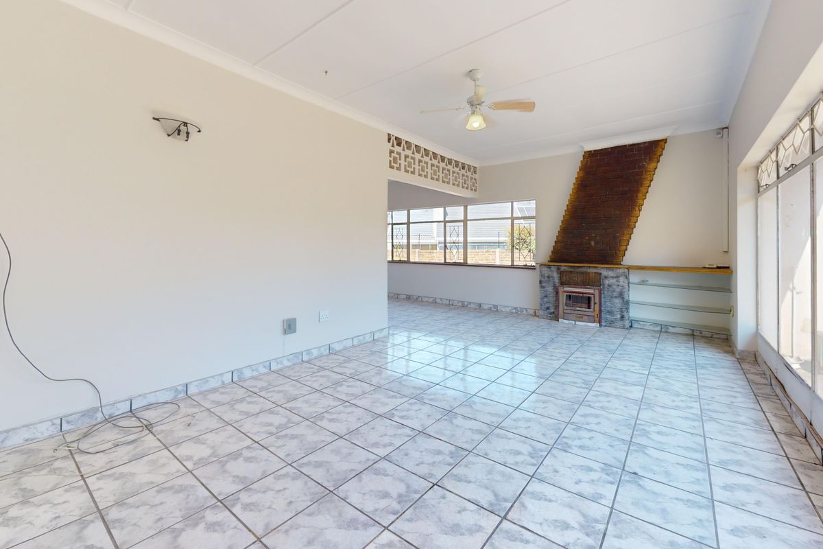 Spacious, light-filled living area featuring tiled flooring, a built-in fireplace, and a decorative breeze block partition, offering a blank canvas for renovation.