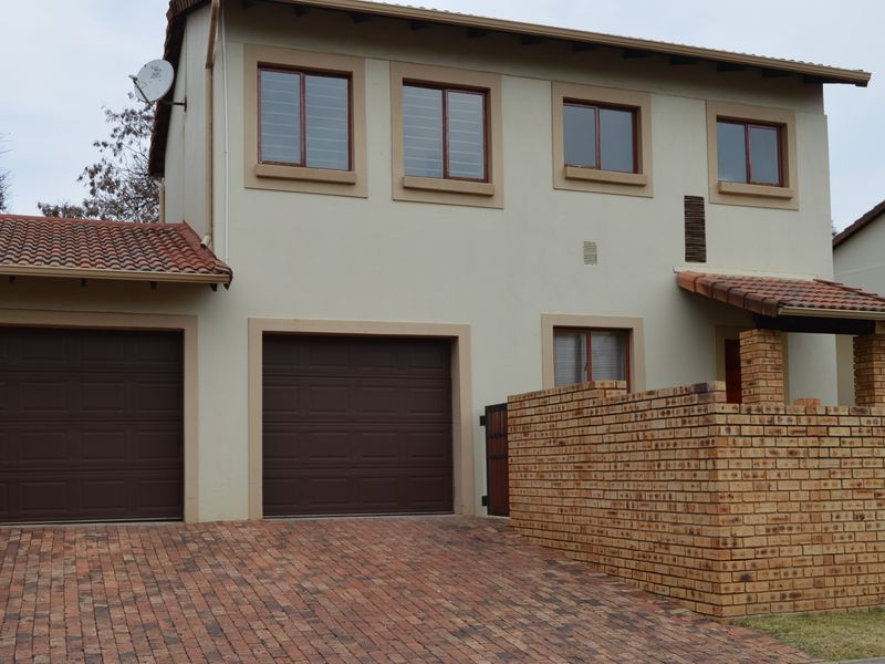 Front elevation of a double-storey townhouse featuring a double garage, brick paved driveway, and a facebrick boundary wall.