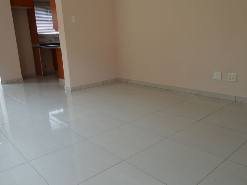 An empty open-plan living area featuring neutral walls, polished ceramic floor tiles, and a glimpse into the adjacent kitchen space.