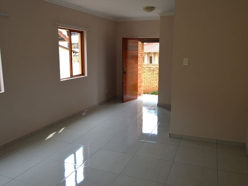 An empty, well-lit living area featuring neutral walls, polished tiled flooring, and wooden window frames, providing a clean and versatile space.