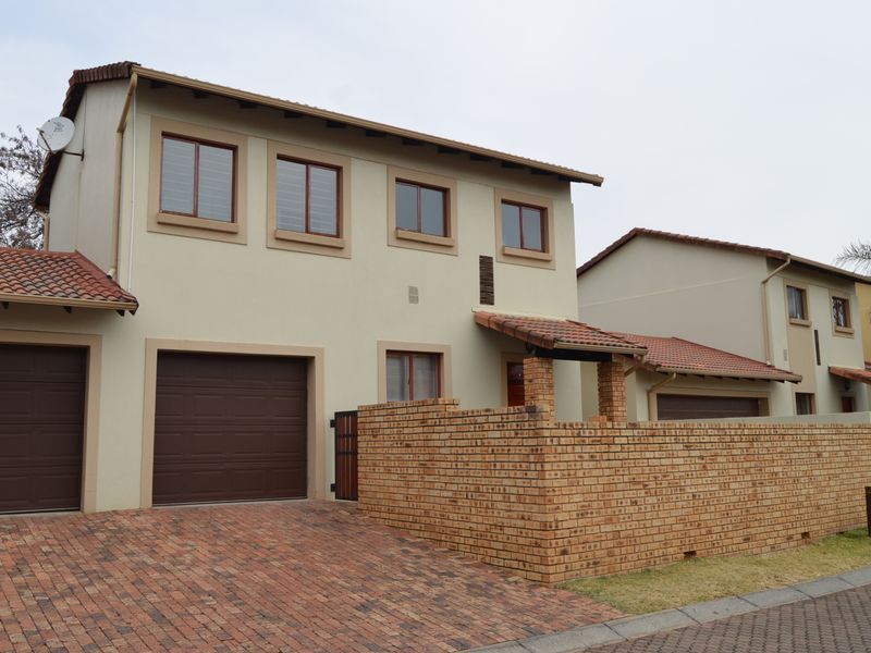 Front elevation of a double-story townhouse featuring a brick driveway, double and single garages, and a face brick boundary wall.