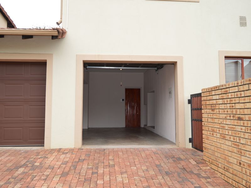 Exterior view of a townhouse garage featuring a brick driveway, a sectional garage door, and a brick boundary wall with a timber gate.