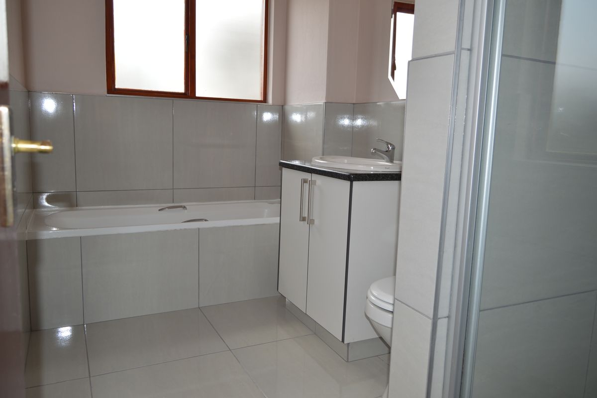 A clean, modern bathroom featuring a built-in vanity, bathtub, separate shower enclosure, and neutral floor-to-ceiling tiling.