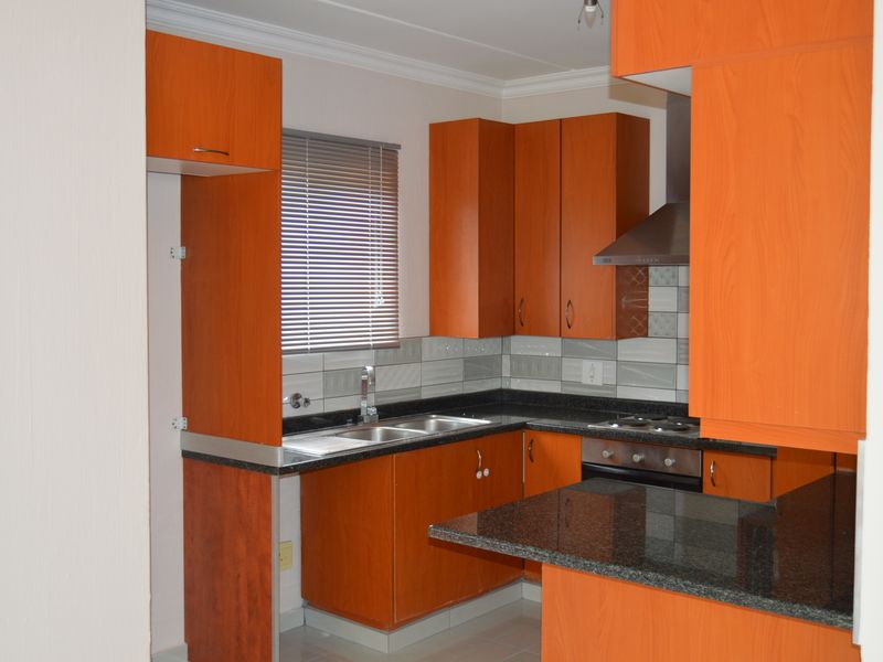 A functional kitchen featuring wood-look cabinetry, granite countertops, built-in oven, hob, and extractor fan, with a tiled backsplash and neutral flooring.