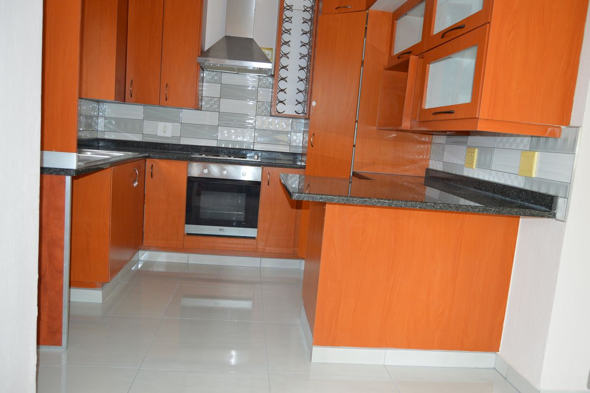 A clean, functional kitchen featuring wood-finish cabinetry, granite countertops, a built-in oven, and a stainless steel extractor fan with modern tiled backsplash.