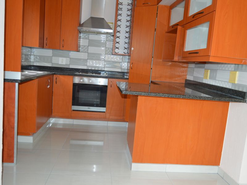 A clean, functional kitchen featuring wood-finish cabinetry, granite countertops, a built-in oven, and a stainless steel extractor fan with modern tiled backsplash.