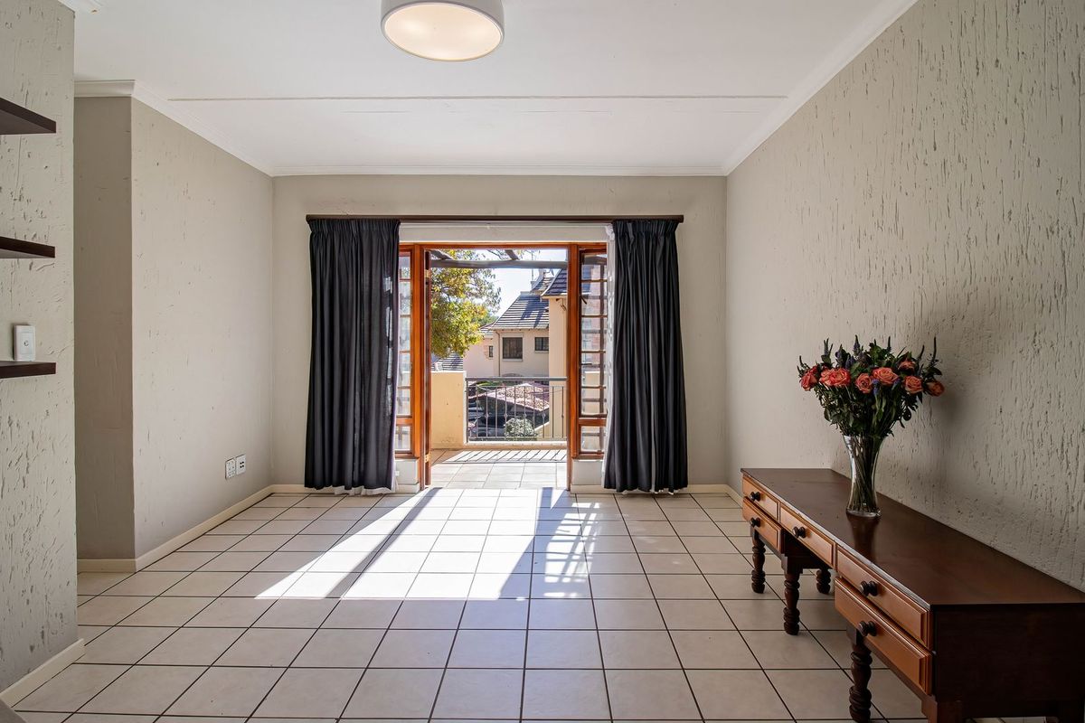Bright and spacious living area featuring neutral tiled flooring, built-in shelving, and direct access to an outdoor balcony through double wooden doors.