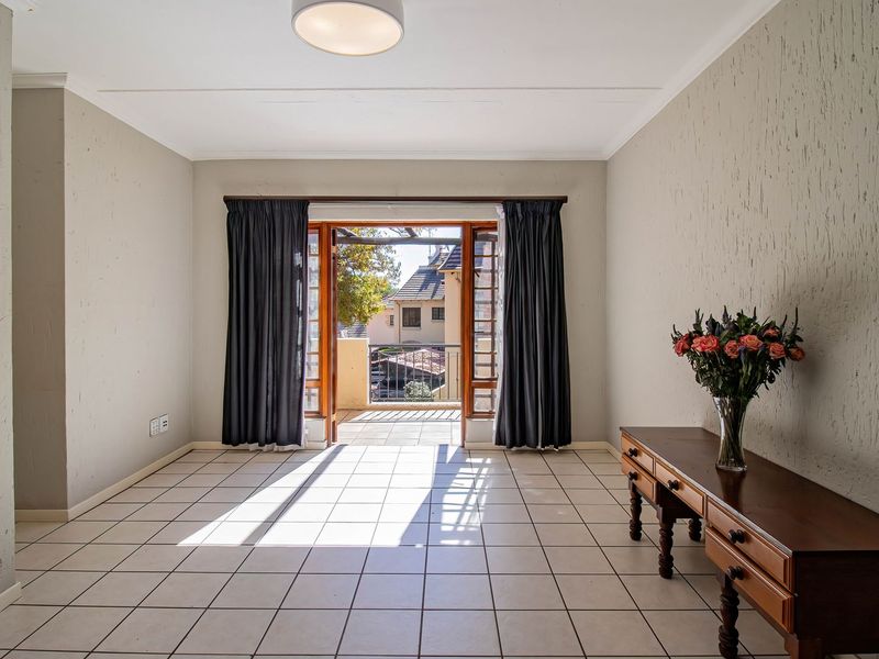 Bright and spacious living area featuring neutral tiled flooring, built-in shelving, and direct access to an outdoor balcony through double wooden doors.