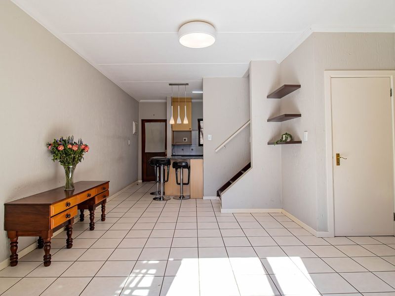 Open plan living area featuring tiled flooring, a staircase with built-in shelving, and a functional kitchen with a breakfast counter.