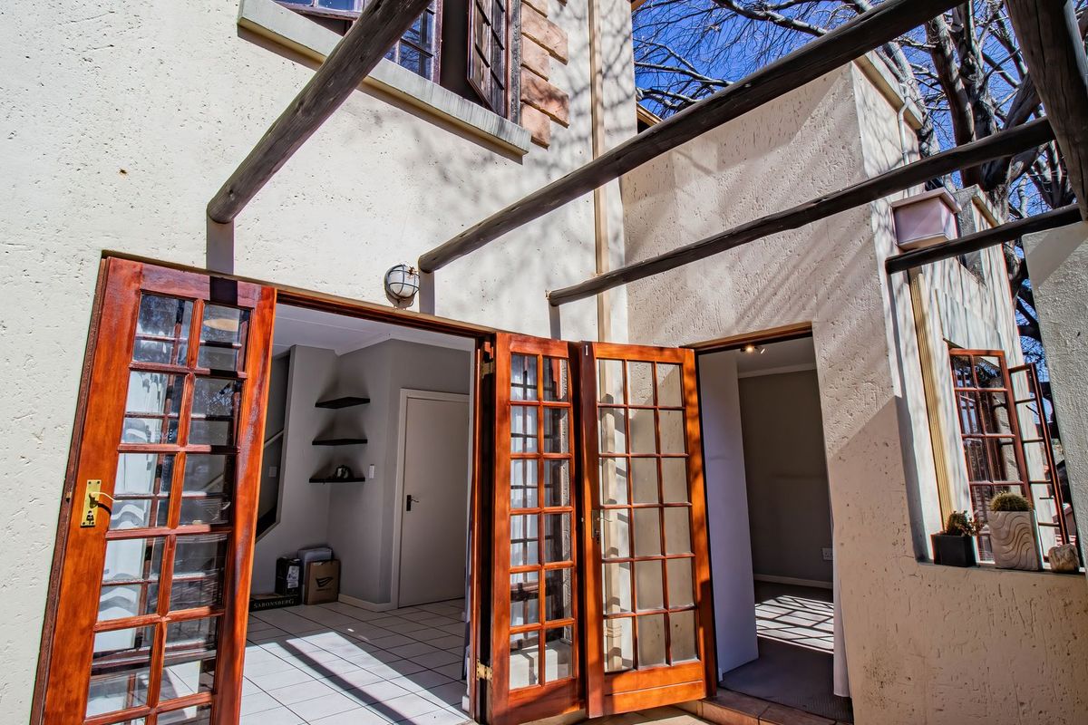 Rear exterior view of the apartment featuring a timber pergola structure and wooden french doors leading into the interior living spaces.