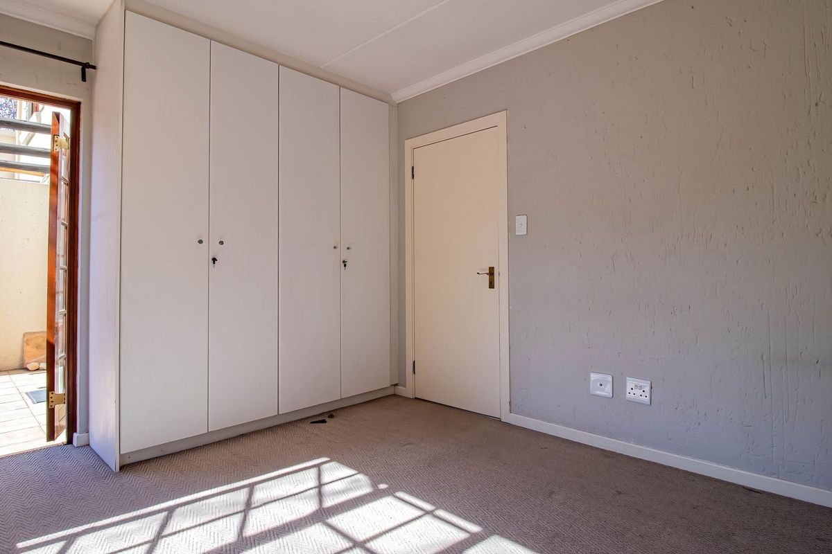 A vacant bedroom featuring built-in cupboards, carpeted flooring, and direct access to an outdoor patio area.