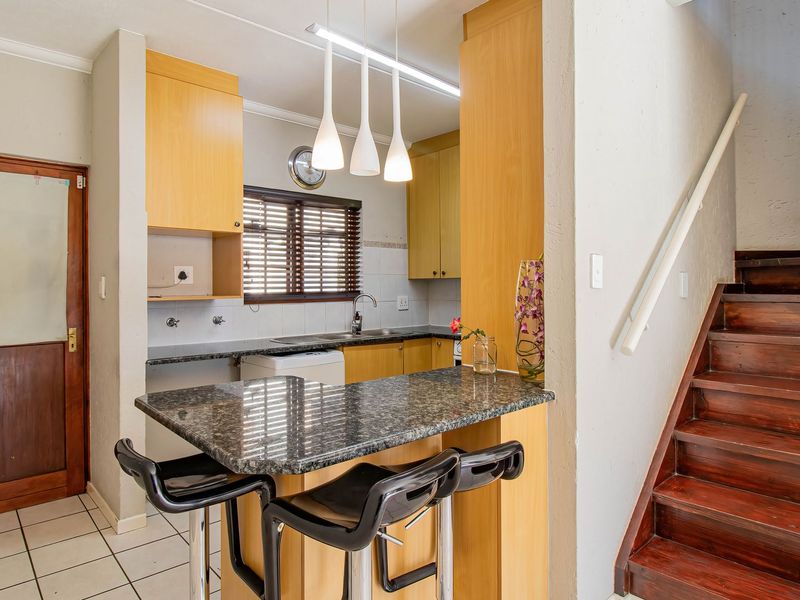 A compact kitchen featuring granite countertops, wooden cabinetry, and a breakfast bar, adjacent to a wooden staircase in an open-plan layout.