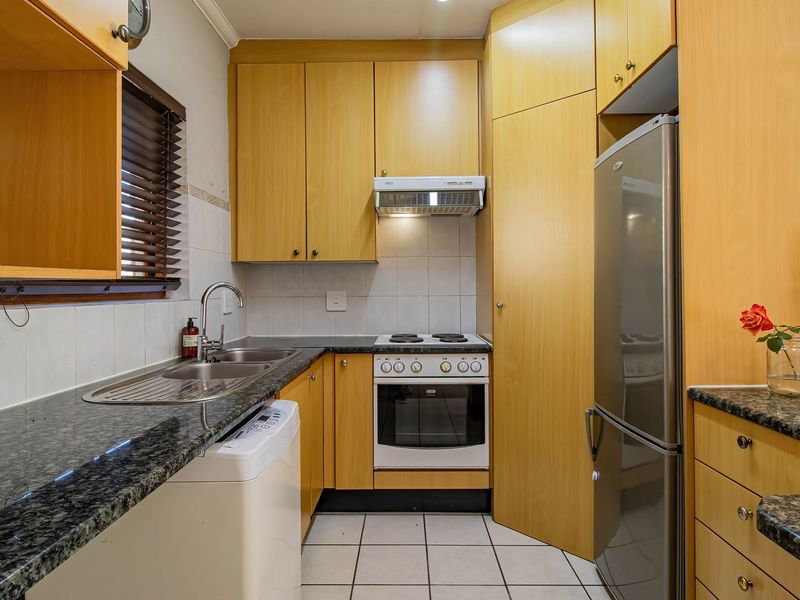 Compact kitchen featuring granite countertops, built-in wooden cabinetry, integrated oven and hob, and tiled flooring with a functional layout.