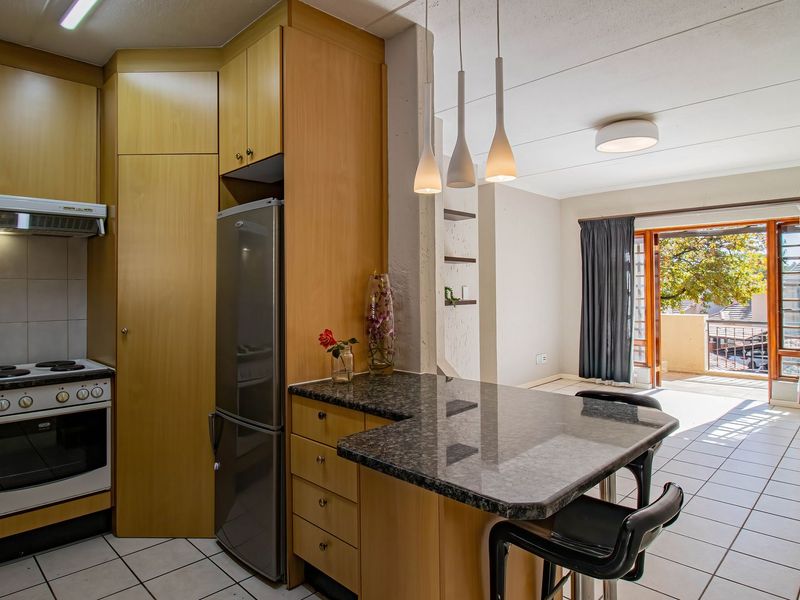Open-plan kitchen and living area featuring laminate cabinetry, granite countertops, tiled flooring, and direct access to a balcony through sliding glass doors.