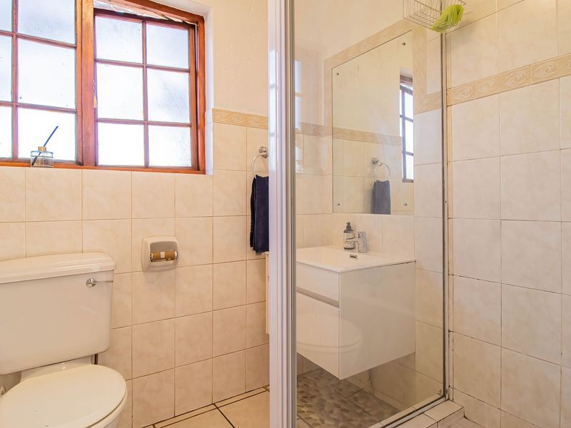 A functional bathroom featuring a shower enclosure, vanity basin, wall-mounted mirror, and tiled finishes with natural light from a timber-framed window.