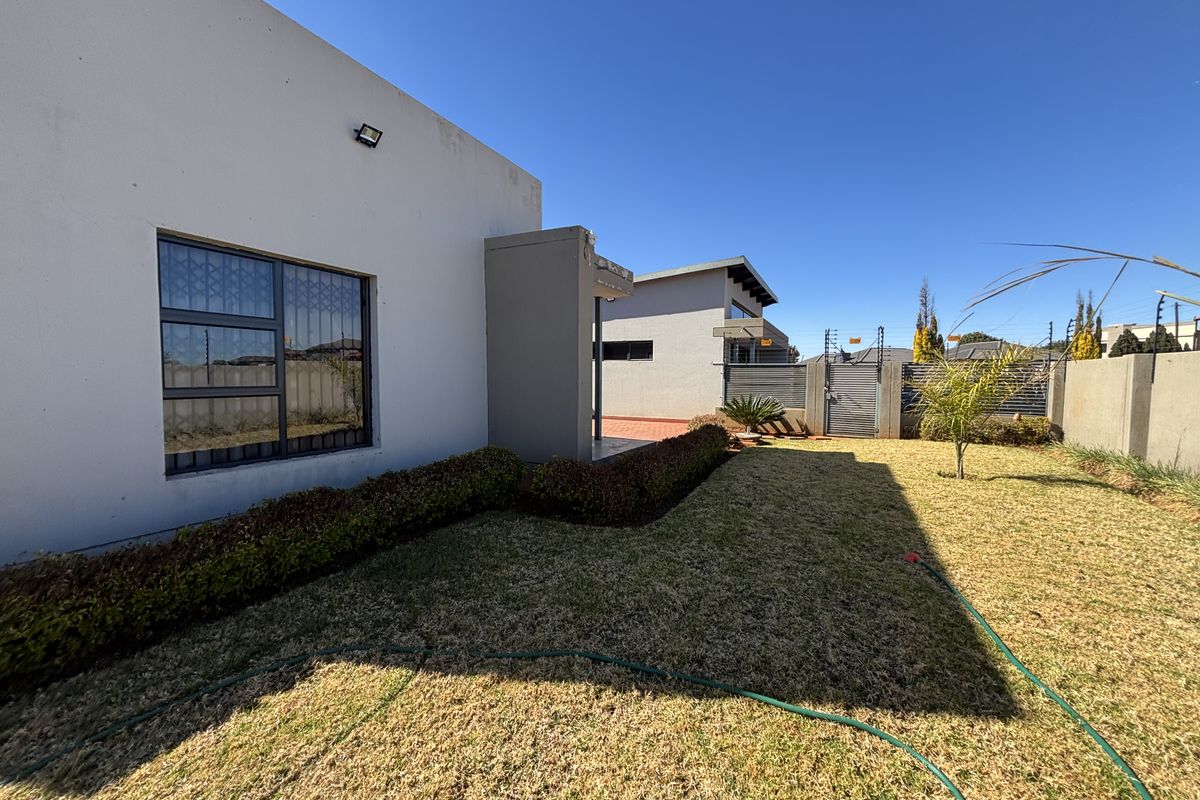 Rear exterior view of the property featuring a lawn, perimeter wall with electric fencing, and security features on the building facade.