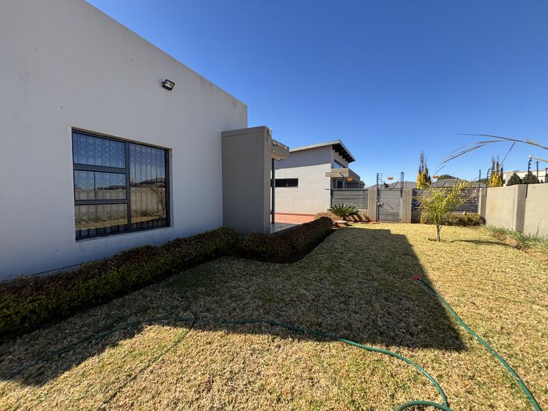 Rear exterior view of the property featuring a lawn, perimeter wall with electric fencing, and security features on the building facade.