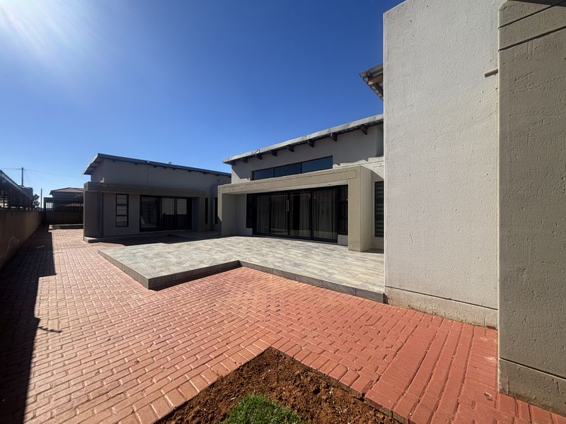 A modern rear exterior view featuring a tiled patio area, brick paving, and large sliding glass doors leading into the home.