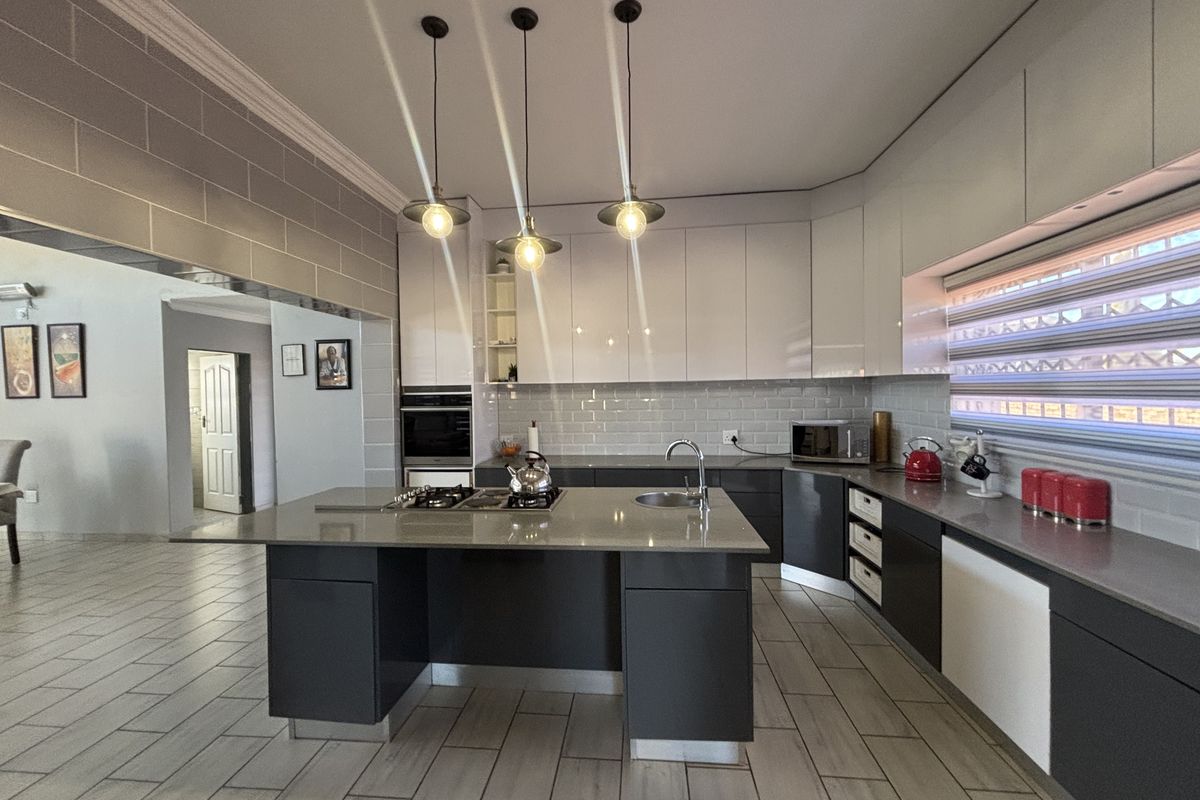 Modern kitchen featuring a central island with gas hob, stone countertops, sleek cabinetry, and contemporary pendant lighting, seamlessly integrated with the living area.