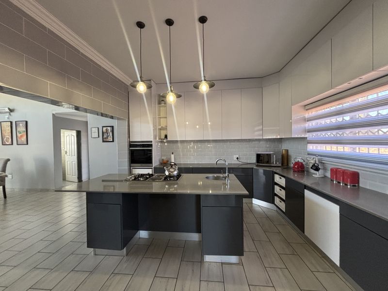 Modern kitchen featuring a central island with gas hob, stone countertops, sleek cabinetry, and contemporary pendant lighting, seamlessly integrated with the living area.