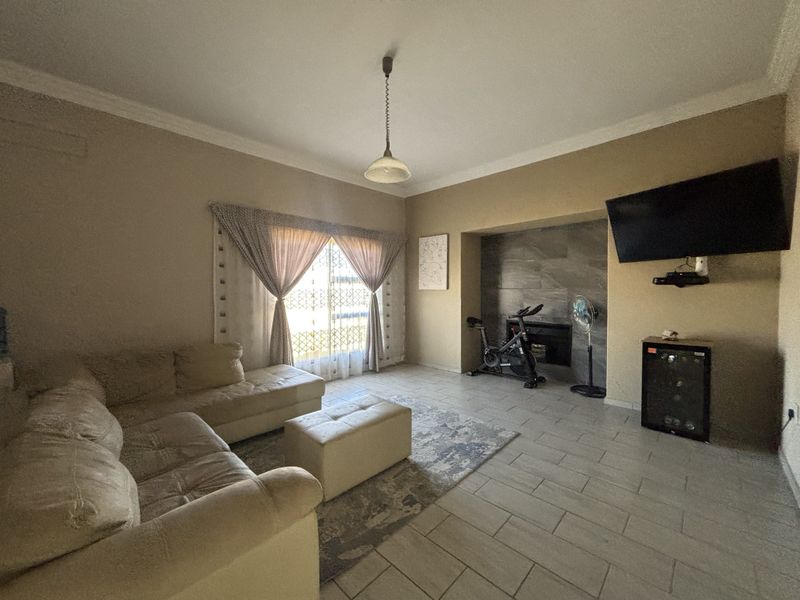 A spacious living room featuring tiled flooring, a stone-clad fireplace feature wall, and decorative cove cornicing.