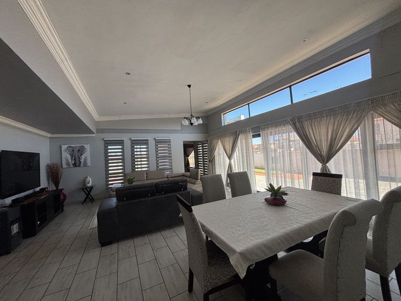 Spacious open-plan living and dining area featuring tiled floors, high ceilings with decorative cornices, and large windows that provide abundant natural light.