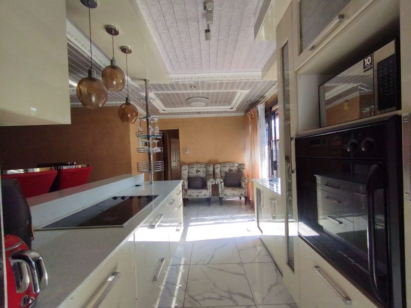 Modern kitchen featuring high-gloss cabinetry, stone countertops, integrated appliances, and elegant coffered ceilings with stylish pendant lighting.