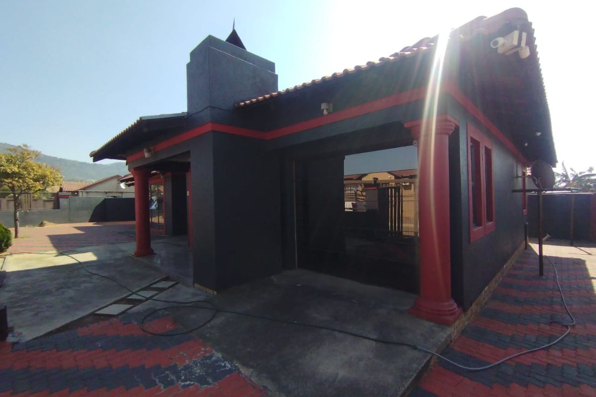 Rear view of the property featuring a tiled roof, decorative columns, and paved outdoor area with an external chimney.