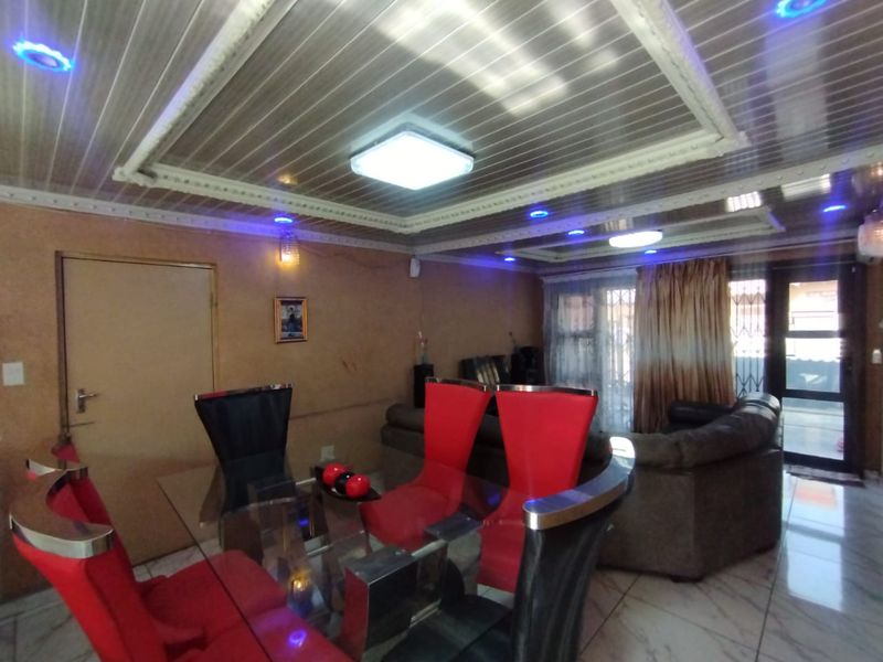 Living and dining area featuring tiled flooring, decorative ceiling panels with integrated lighting, and access to an outdoor space via a sliding glass door.