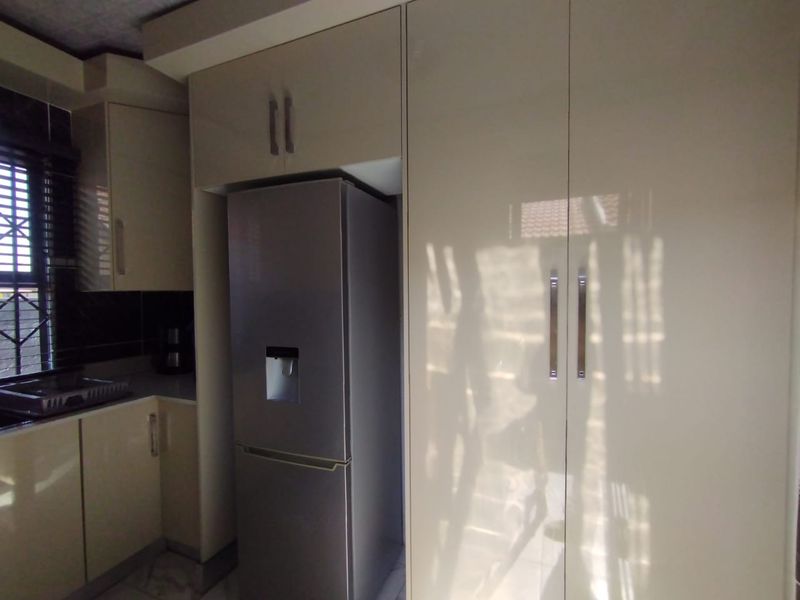 A modern kitchen featuring high-gloss cabinetry, integrated storage, and a tiled backsplash with natural light filtering through a window with security bars.