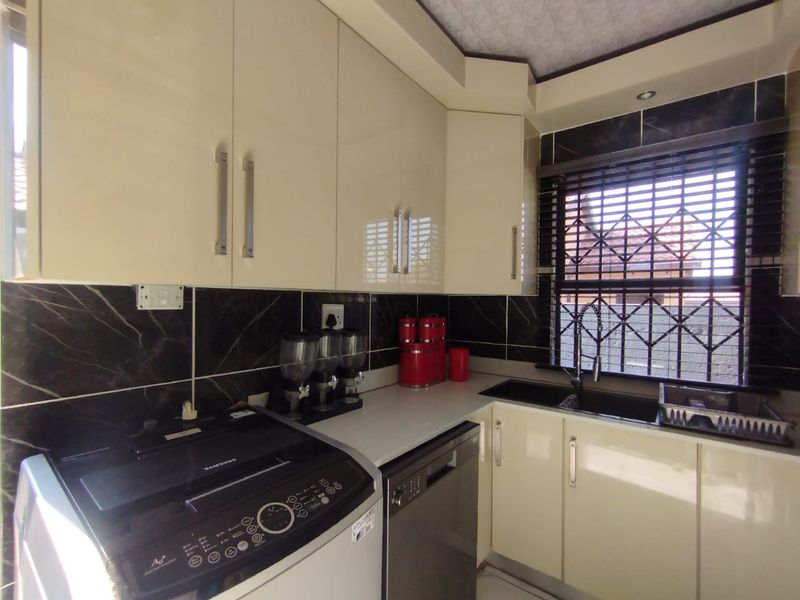 A functional scullery area featuring modern high-gloss cabinetry, dark tiled splashbacks, and a double sink with a window view.