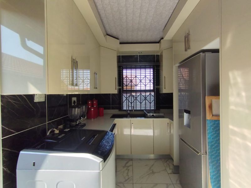 A compact, modern kitchen featuring high-gloss cabinetry, dark tiled backsplash, marble-look floor tiles, and a functional sink area with window security.