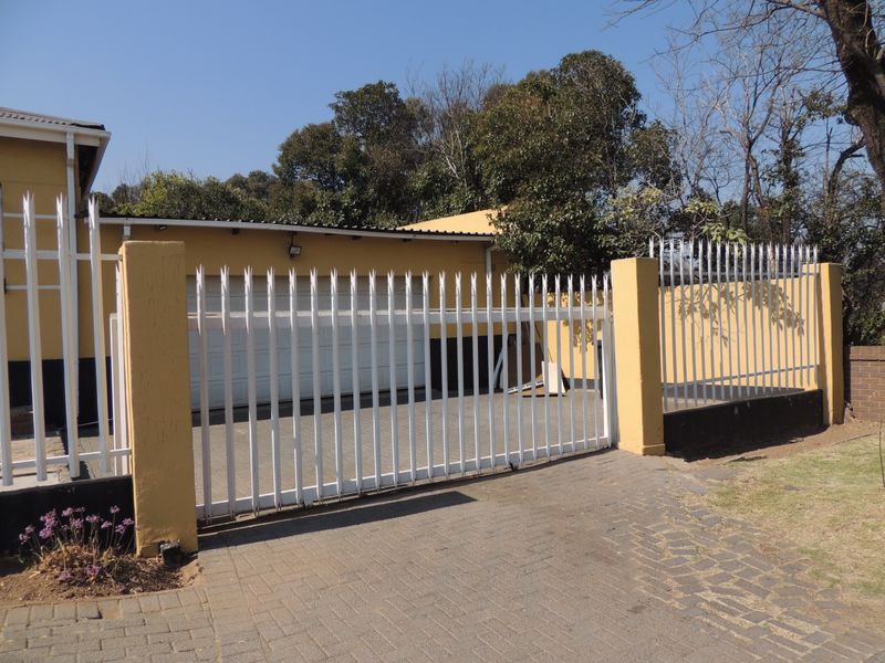 Front exterior view featuring a paved driveway, secure metal gate, and garage access with perimeter walling.