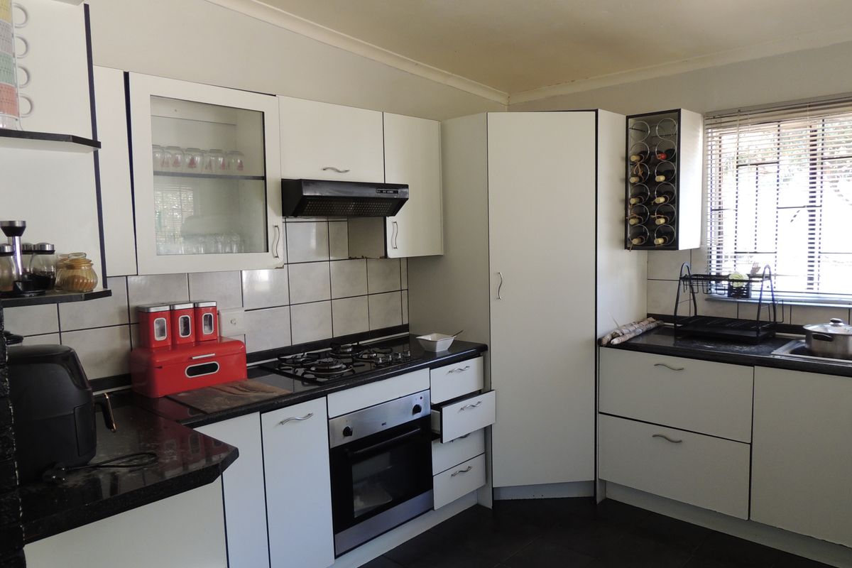 Functional kitchen featuring white cabinetry, granite countertops, gas hob, built-in oven, and tiled backsplash with a window providing natural light.
