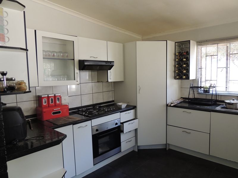 Functional kitchen featuring white cabinetry, granite countertops, gas hob, built-in oven, and tiled backsplash with a window providing natural light.