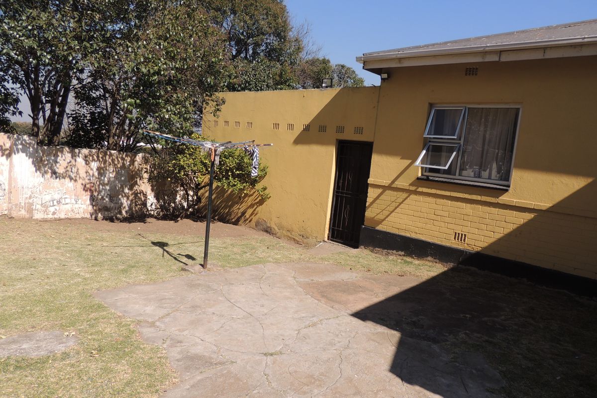 Rear exterior view of the property featuring a paved patio area, security gate, and brick boundary wall.