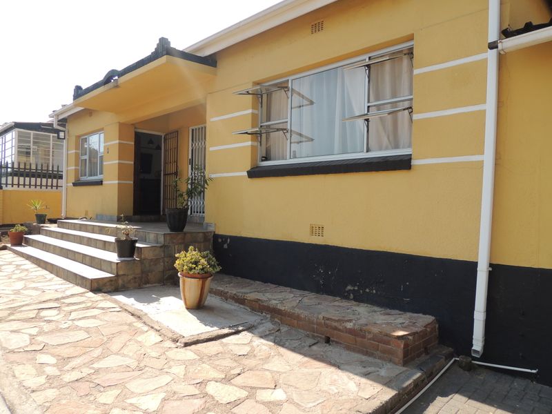Front elevation of a single-story house featuring yellow plastered walls, tiled entrance steps, and stone paving.
