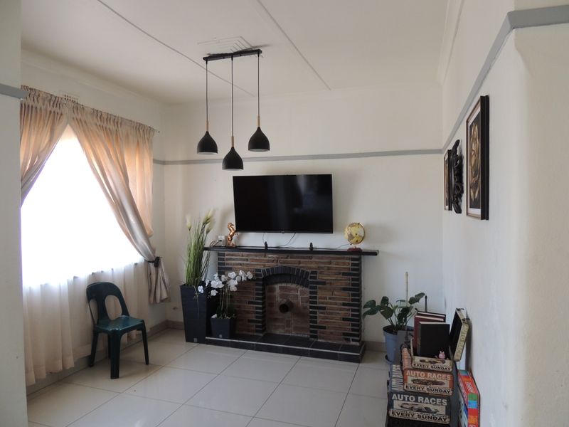 Living room featuring a brick fireplace, tiled flooring, and modern pendant lighting, providing a functional space with classic architectural details.