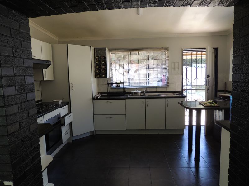A functional kitchen featuring built-in cabinetry, a gas hob, oven, and direct access to the rear exterior through a security gate.