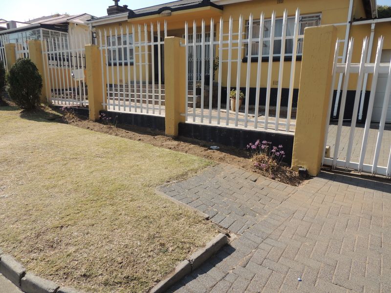 Front view of the property featuring a paved driveway, lawn, and secure perimeter fencing with concrete pillars.